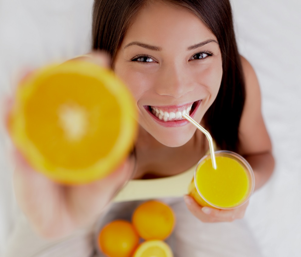 Woman drinking orange juice smiling showing oranges. Young beautiful mixed-race Asian / Caucasian model.
